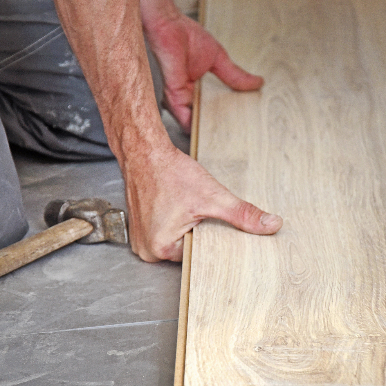 Professional Laminate Flooring Installation | Seamless and Precise Flooring Services A worker connecting laminate flooring pieces by hand, showcasing the precision of professional flooring installation.